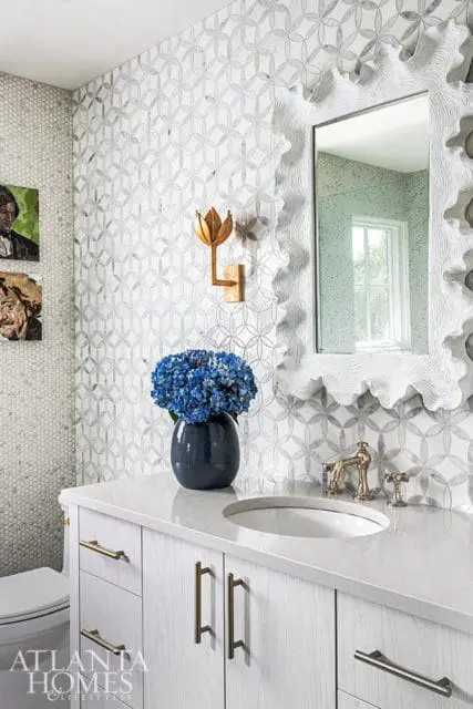 Powder room with geometric marble tile, white vanity, brass fixtures, and blue hydrangeas