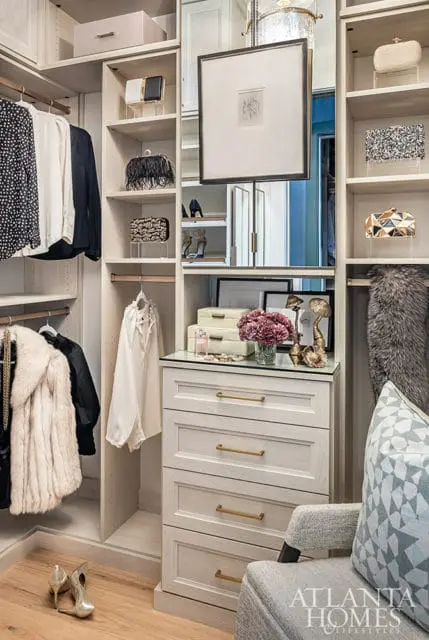 Walk-in closet with white cabinetry, gold hardware, and clothing.