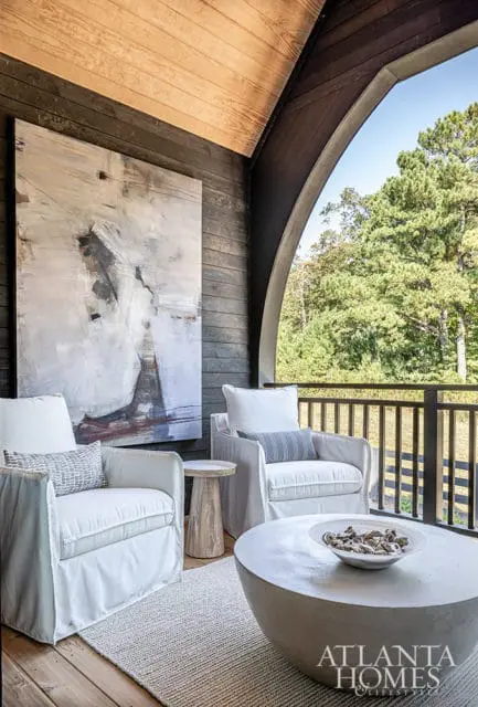 Covered porch with two white slipcovered chairs, abstract art, and concrete coffee table.