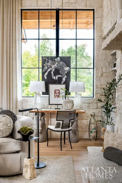 Living room with stone accent wall, large window, console table with art and lamps, and seating.