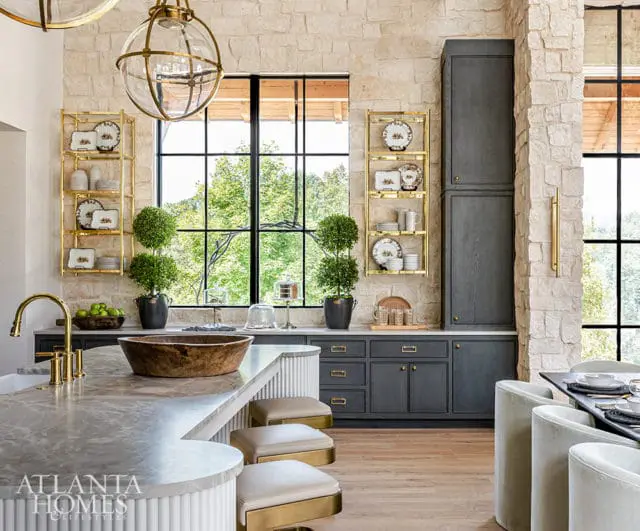 Kitchen with stone walls, dark gray cabinets, marble island, and gold shelving.
