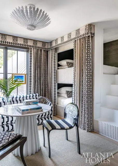 Bunk beds with patterned curtains, white table, striped chair, and ceiling light