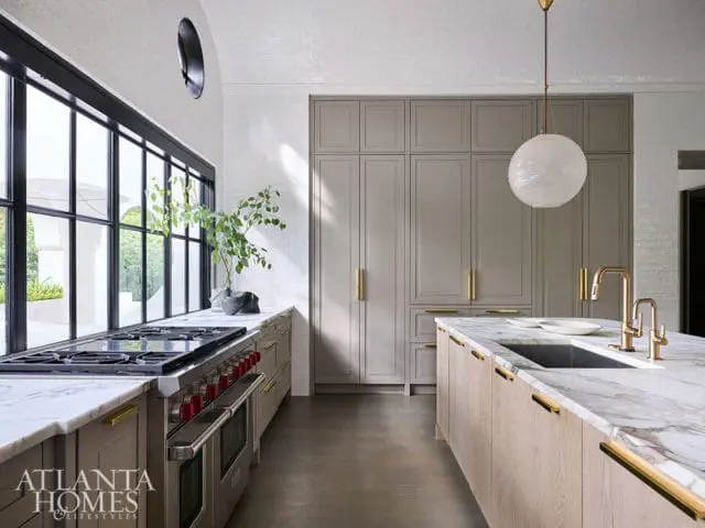 Modern kitchen with marble island, gray cabinetry, and large windows.