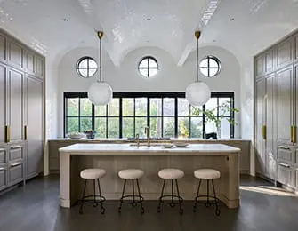 Kitchen with light gray cabinetry, white marble island with bar stools, and arched windows