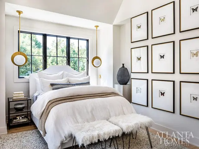 Bedroom with white bedding, gold pendant lights, and framed butterfly art.