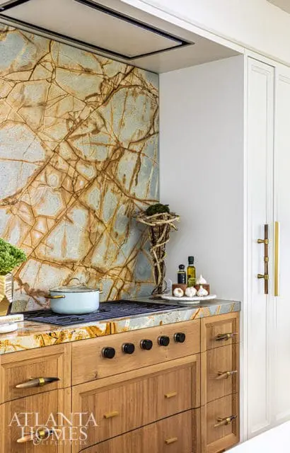 Kitchen with a dramatic stone backsplash, wood cabinetry, and brass hardware.