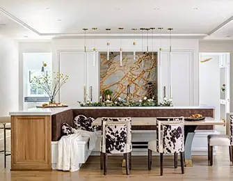 Kitchen island with marble backsplash, cowhide chairs, and wooden cabinetry.