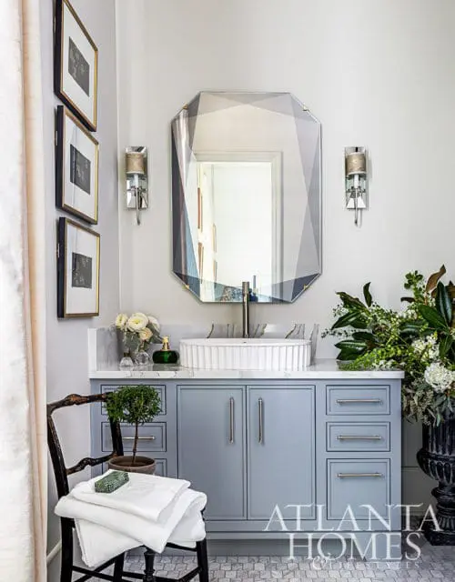 Powder room with light blue vanity, white fluted sink, faceted mirror, and three framed prints.