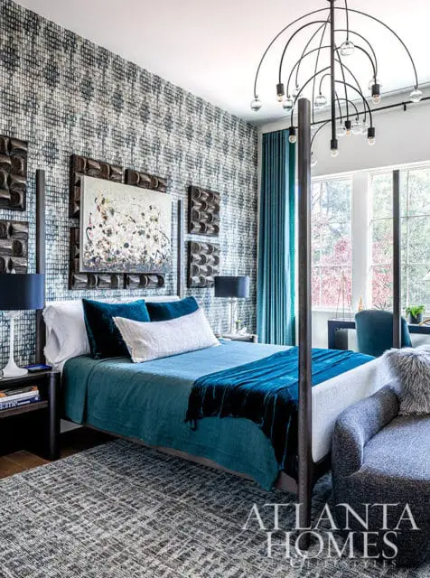 Bedroom with blue patterned wallpaper, teal bedding, abstract art, and modern chandelier.