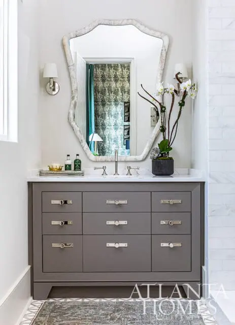 Gray bathroom vanity with marble countertop, ornate mirror, and white orchid arrangement.