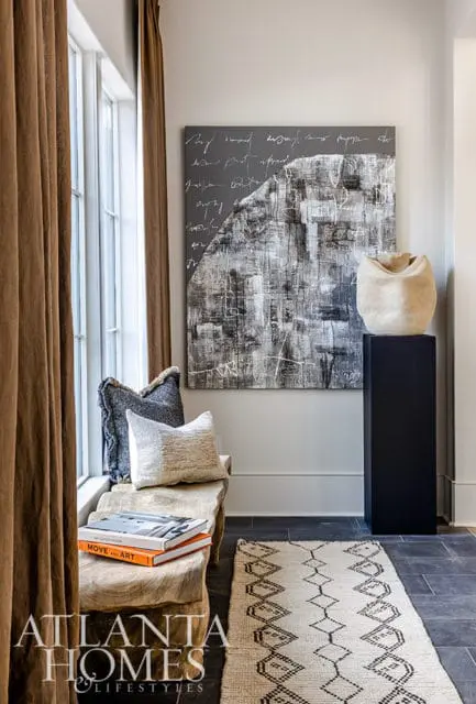 Entryway with wood bench, abstract art, and patterned rug. Atlanta Homes & Lifestyles logo.