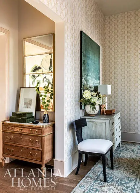 Hallway with patterned wallpaper, antique dresser, mirror, and chair.