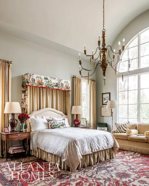 Bedroom with a four-poster bed, ornate chandelier, large windows, and a Persian rug.