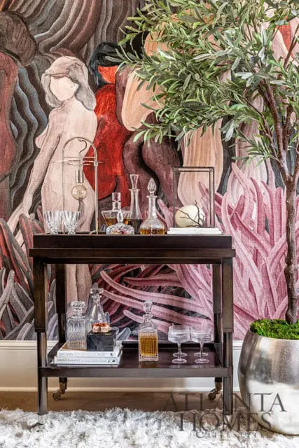 Bar cart with crystal decanters and glasses against a mural of figures.