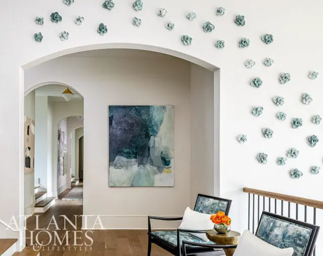 Hallway with abstract art, two chairs, and floral wall decor. Atlanta Homes & Lifestyles logo.
