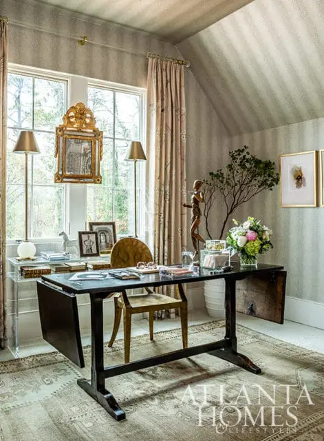 Office with desk, chair, and ornate mirror above window. Striped wallpaper.