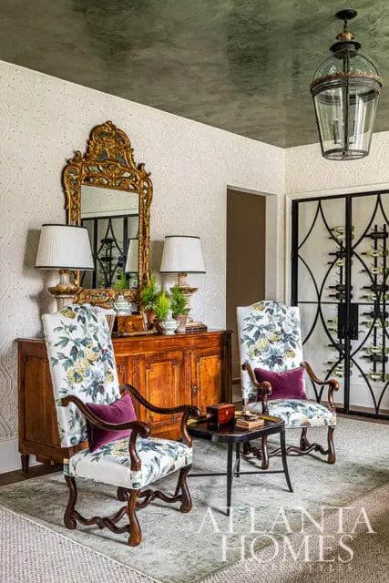 Two armchairs with floral upholstery flank a wooden cabinet topped with lamps and plants.