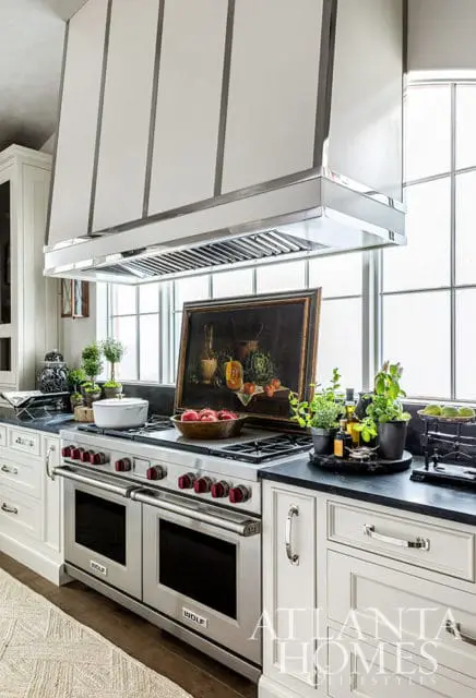 Kitchen with stainless steel range, white cabinetry, and a still life painting on the stovetop.