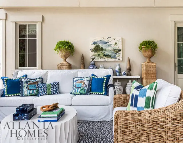 White sofa with blue and green patterned pillows, rattan armchair, and white coffee table.
