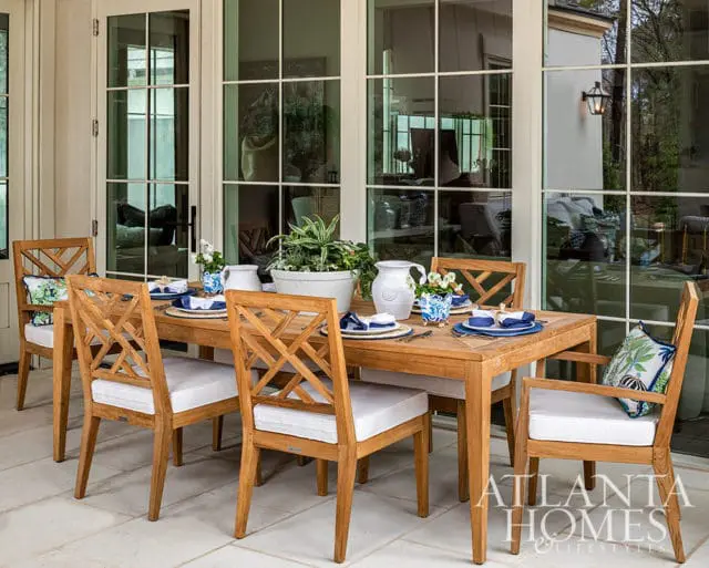 Wooden dining table and chairs with white cushions on a tiled patio.