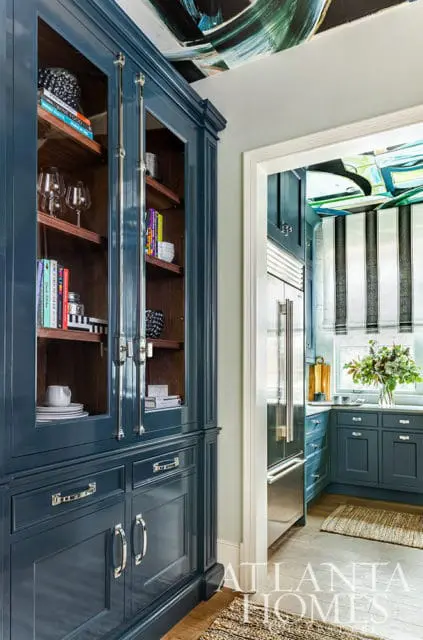Blue built-in cabinetry with glass doors and wooden shelves, leading to a kitchen with stainless