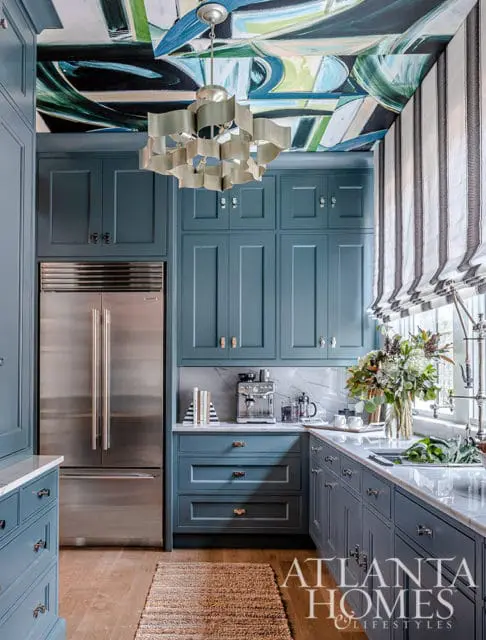 Blue kitchen with marble countertops, stainless steel refrigerator, and abstract painted ceiling