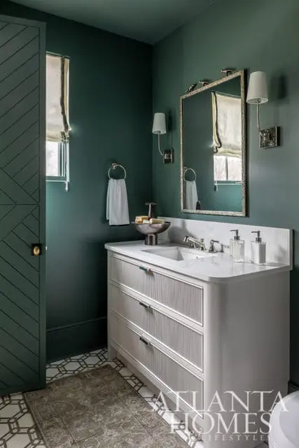 Dark green bathroom with white marble vanity, fluted drawers, ornate mirror, and patterned floor