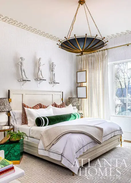 Bedroom with white bed, green bolster pillow, patterned wallpaper, and ornate chandelier.