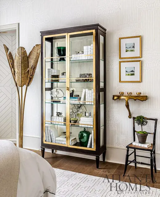 Dark wood curio cabinet with glass doors and brass trim, filled with books and decor.
