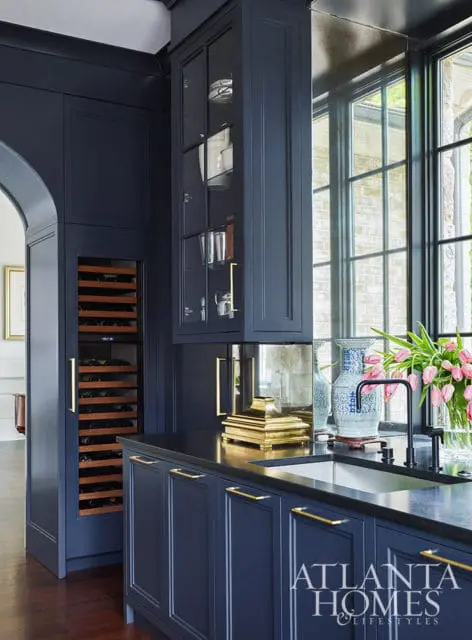 Navy kitchen cabinetry with brass hardware, wine fridge, and sink. Features a blue and white vase
