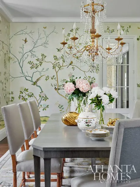 Dining room with Chinoiserie wallpaper, upholstered chairs, and a crystal chandelier.
