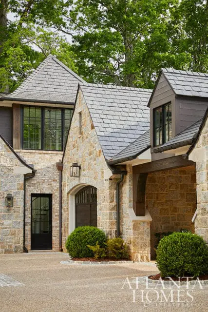Stone and brick house with slate roof, dark windows, and arched garage door.