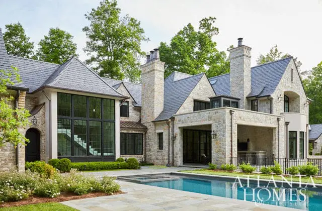 Stone mansion with slate roof, large windows, and swimming pool. Atlanta Homes & Lifestyles logo in