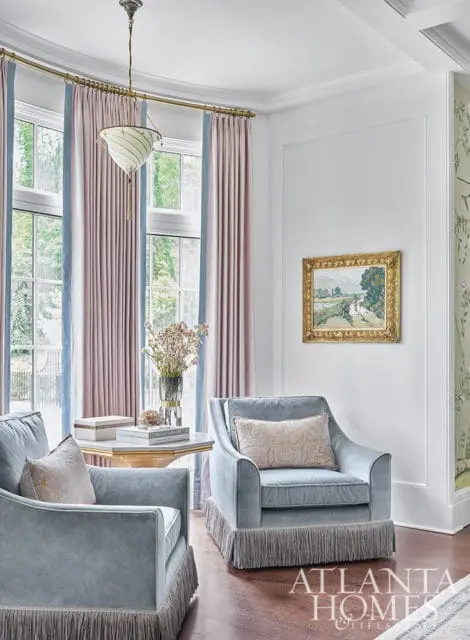 Light blue armchairs with fringed skirts and patterned pillows, next to a table with books and