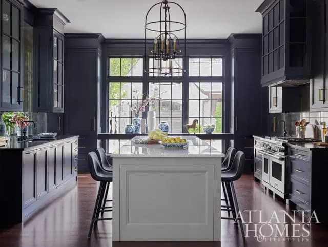Dark blue kitchen with marble island, stainless steel range, and brass hardware.