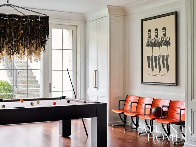 Billiard table, orange stadium seats, and boxing art in a room with a modern chandelier.