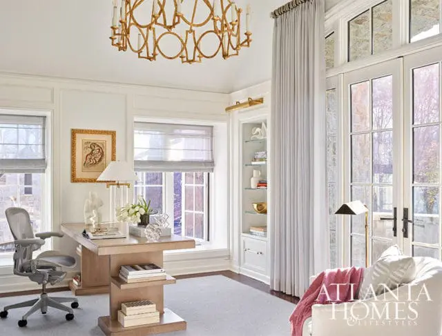 Office with light wood desk, gray chair, built-in shelves, and large windows.