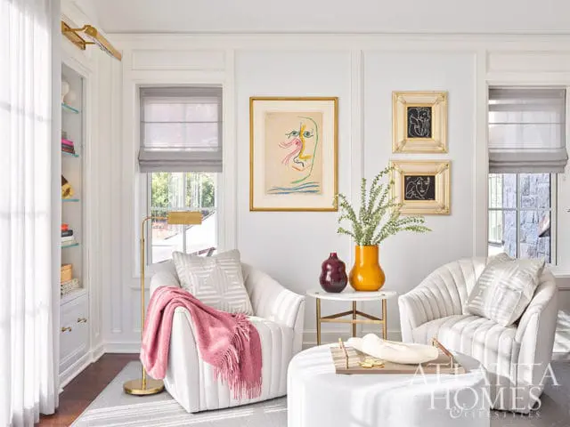 White living room with two armchairs, abstract art, and a pink throw