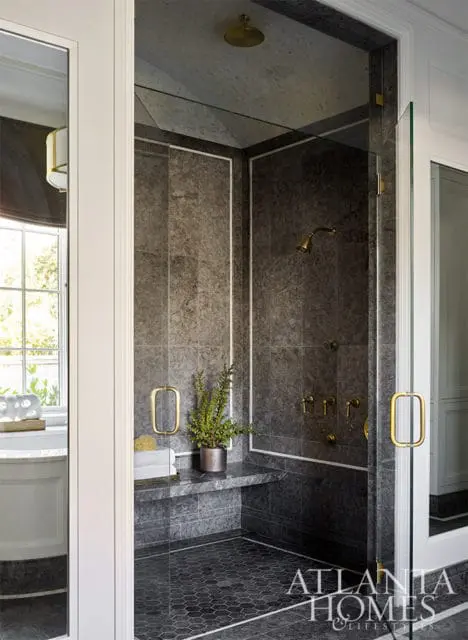 Dark gray tiled shower with brass fixtures, built-in bench, and hexagonal floor tiles.