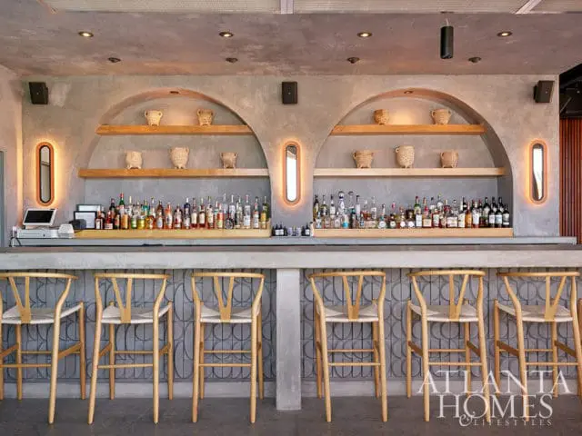 Bar with concrete counter, wooden stools, and shelves stocked with liquor bottles.