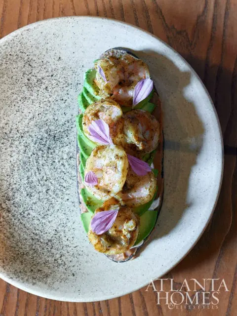 Shrimp and avocado toast on a speckled plate with purple flower petals