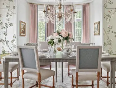Dining room with chinoiserie wallpaper, upholstered chairs, and floral centerpieces.