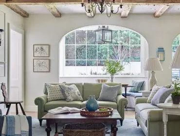 Living room with green sofas, wood beams, arched window, and fireplace