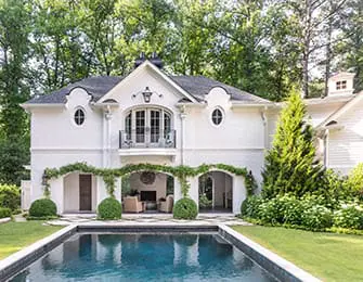 White brick house with arched openings, balcony, and swimming pool in the foreground.
