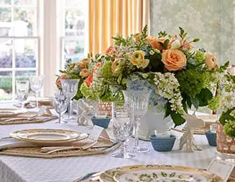 Dining table set with floral centerpiece, crystal glasses, and patterned plates.