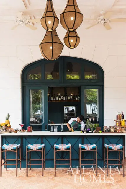Bar with teal cabinetry, white counter, and colorful stools. Bartender works behind counter.