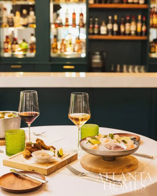 Table setting with two glasses of wine, fried food, and shrimp cocktail in front of a bar.