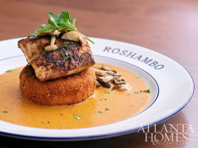 Fried fish on a round cake with sauce and mushrooms, on a plate with Roshambo and Atlanta Homes &