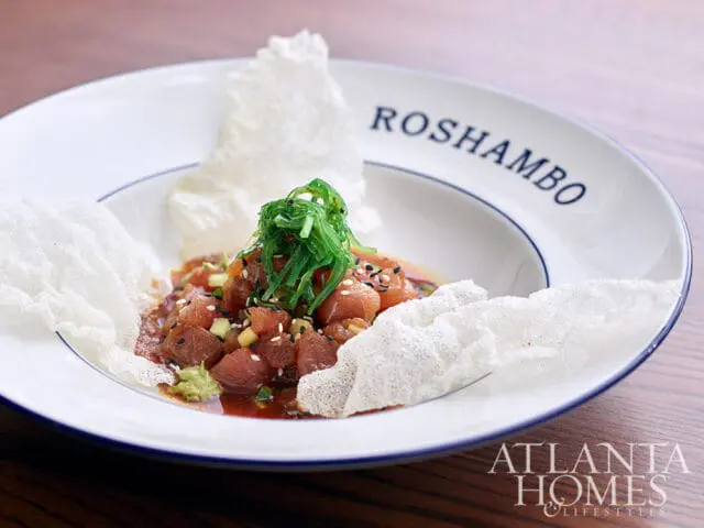 Tuna poke with seaweed salad and crispy wonton chips on a white plate with Roshambo text