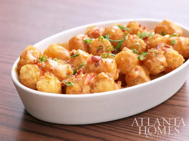 Tater tots topped with cheese sauce, bacon bits, and chives in a white oval bowl